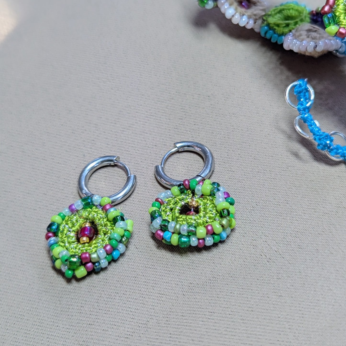 Flat lay of Vana bead crochet earrings with circular floral design, green and blue glass seed beads, sustainable jewellery.