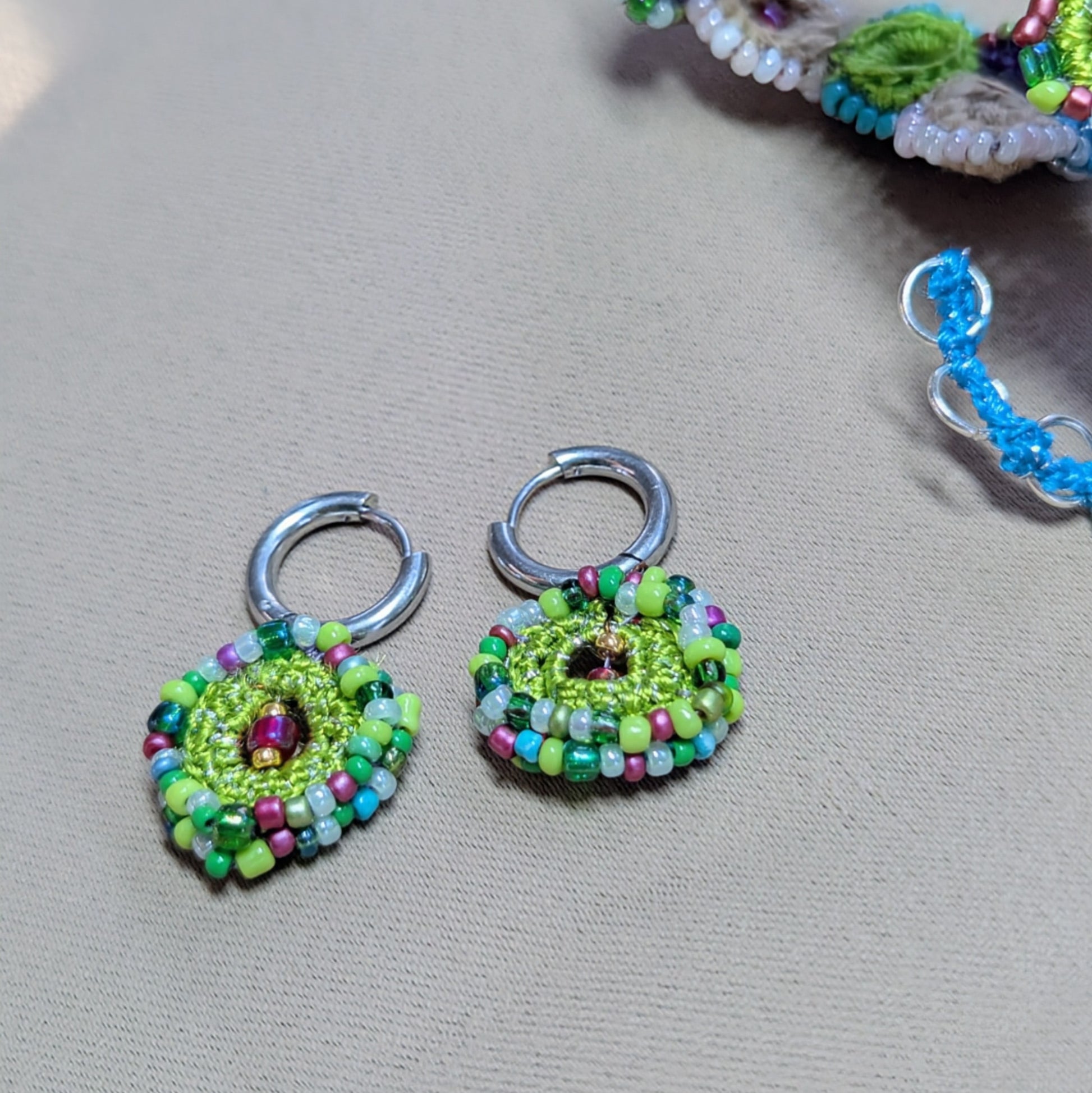 Flat lay of Vana bead crochet earrings with circular floral design, green and blue glass seed beads, sustainable jewellery.