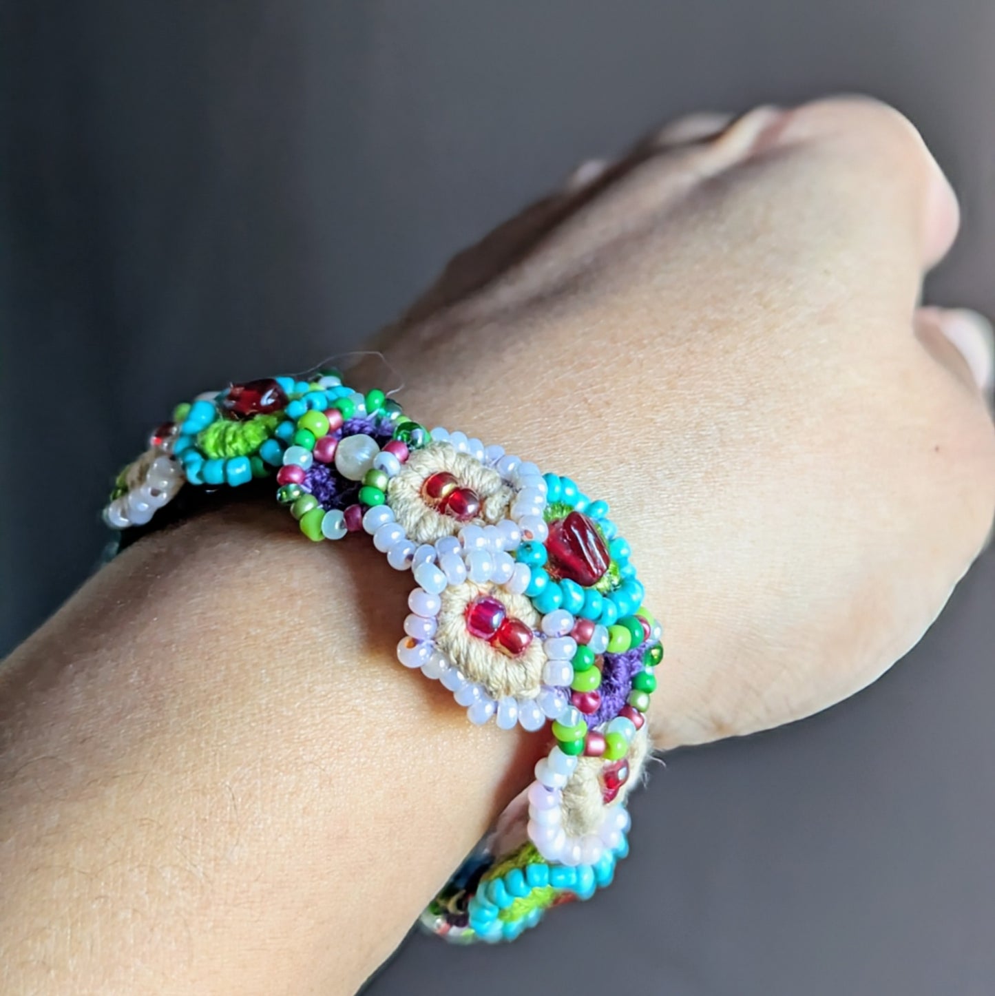 Side view of a handcrafted garden-inspired bracelet modelled on a wrist, featuring turquoise, green, purple, and red vintage glass beads accented with seed pearls, created by UK Indian designer Megha.