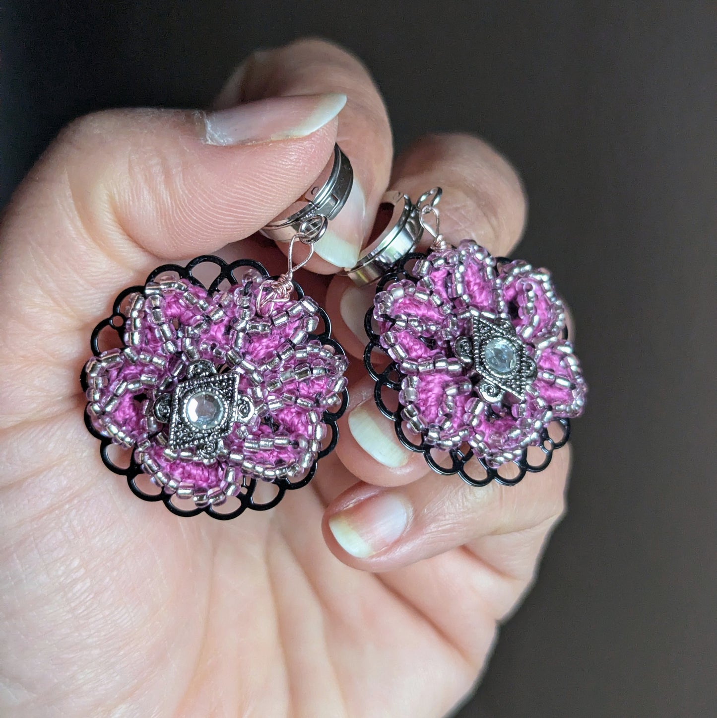 Handmade pink floral earrings with silver lined Japanese beads and filigree detail displayed in hand.