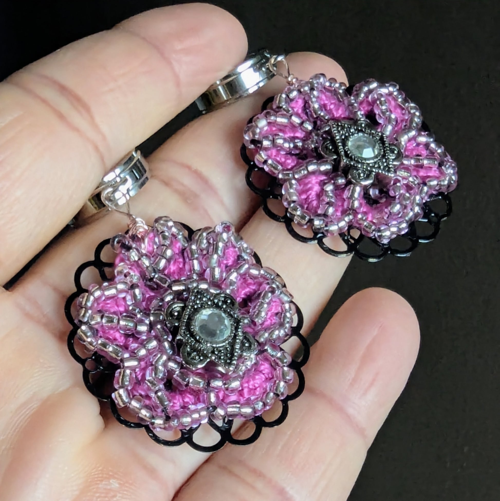 Angled view of pink and silver artisan earrings revealing dimensional crochet and wire detail.