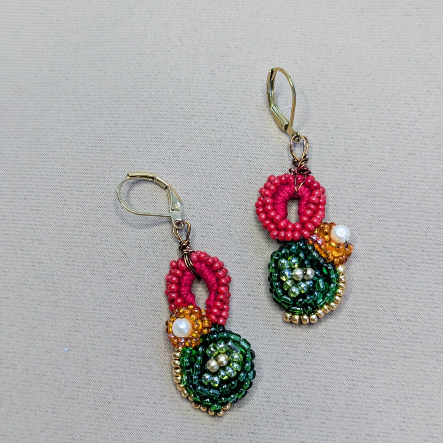 Vasanta red green and gold handmade floral beaded earrings on neutral fabric backdrop.