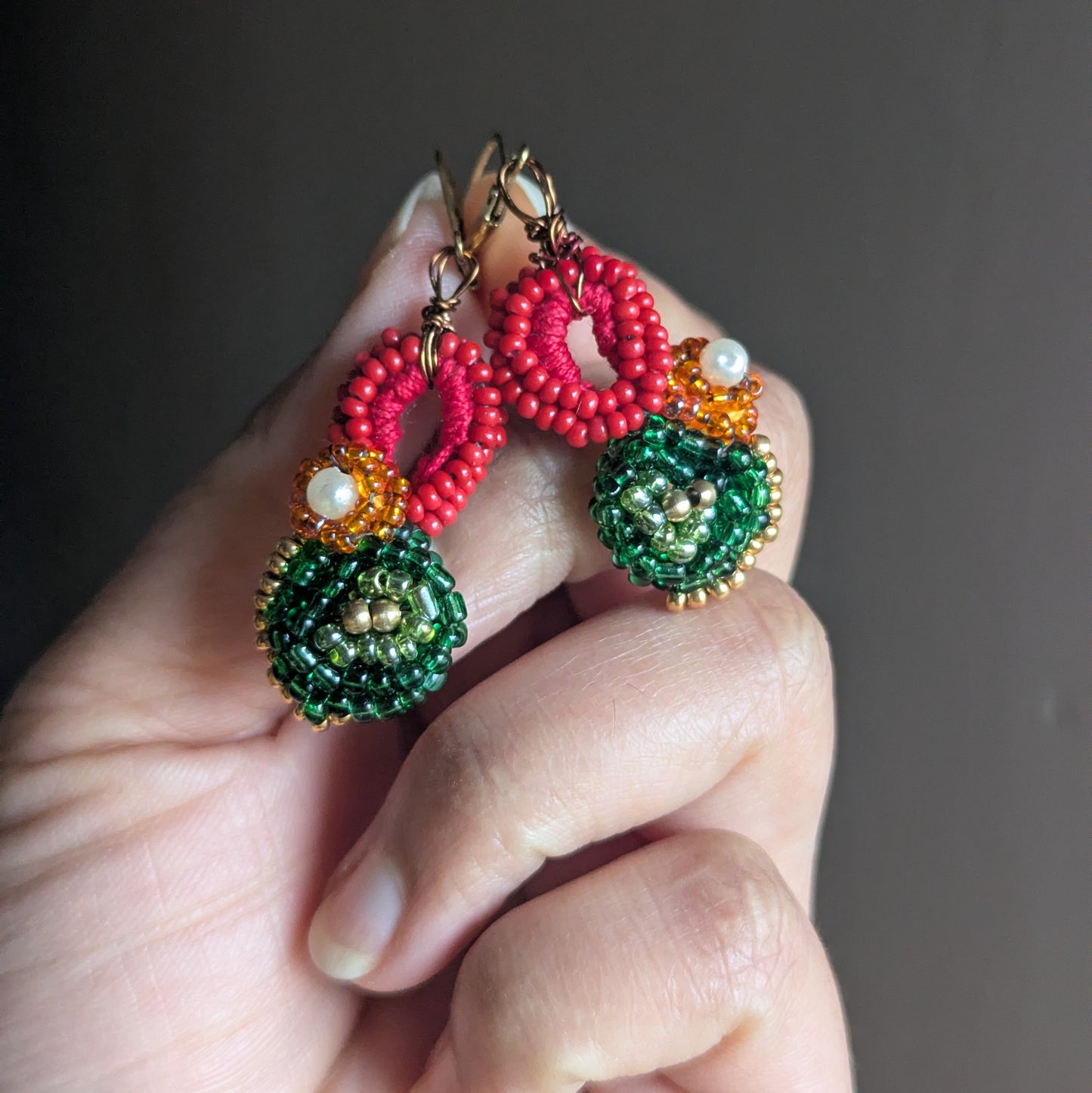 Close-up view of Vasanta artisan handmade red green and gold floral beaded Indian style earrings UK.
