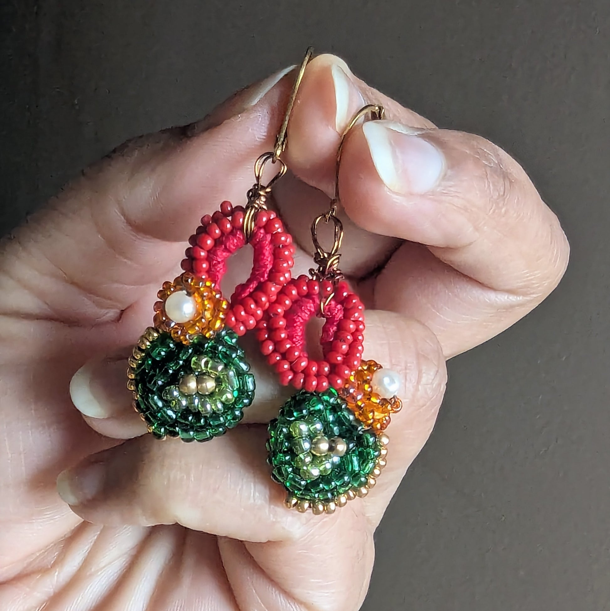 Lightweight red green gold beaded earrings handmade in the UK displayed in hand.