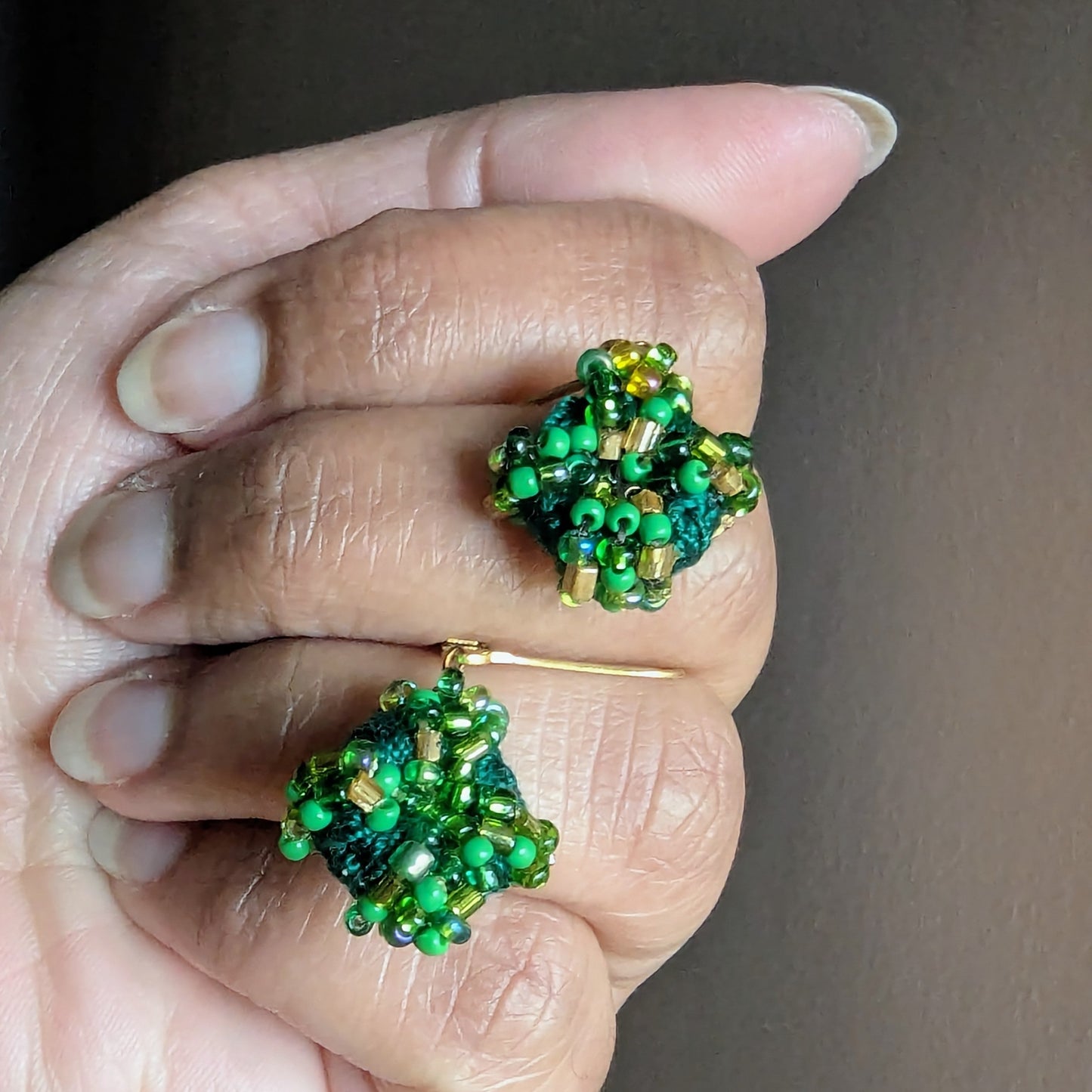 Hand holding a pair of green and gold homemade artisan earrings designed exclusively for Mayaani Jewellery.