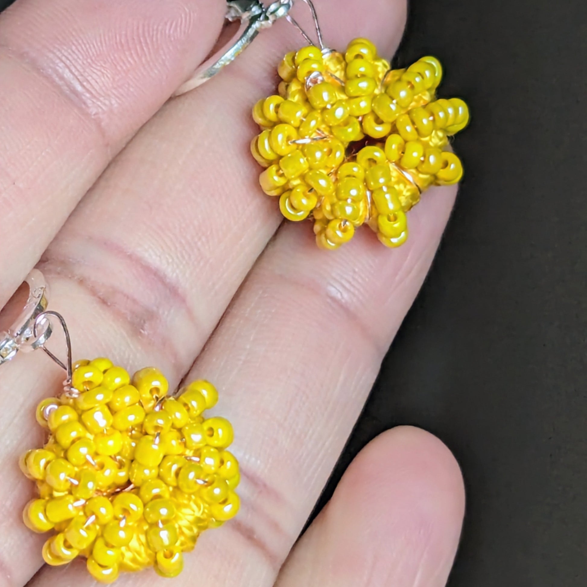 Hand holding a unique artisan made pair of yellow seed bead earrings featuring high quality materials curated.