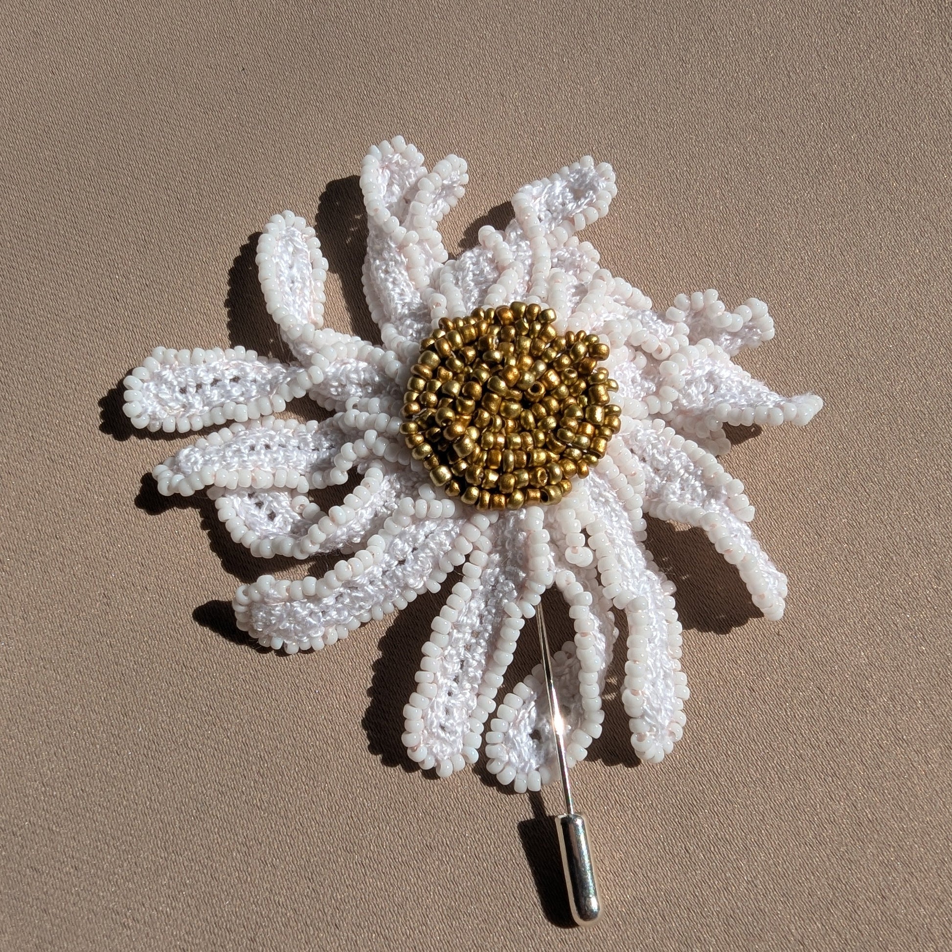 Flat lay image of a sun kissed daisy flower brooch pin exclusively handmade in the UK using hand crochet and hand bead embroidery techniques unique to Mayaani Jewellery UK.