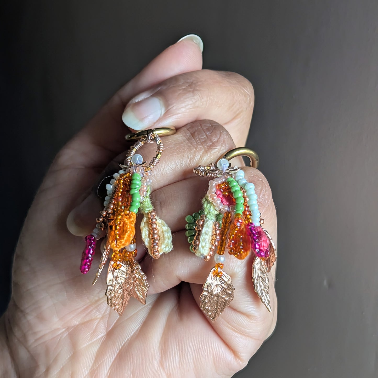 Handheld photo of Zariya one-of-a-kind beaded tassel earrings with rose gold leaf charms, seed pearls and pastel Czech glass beads on gold hoops.
