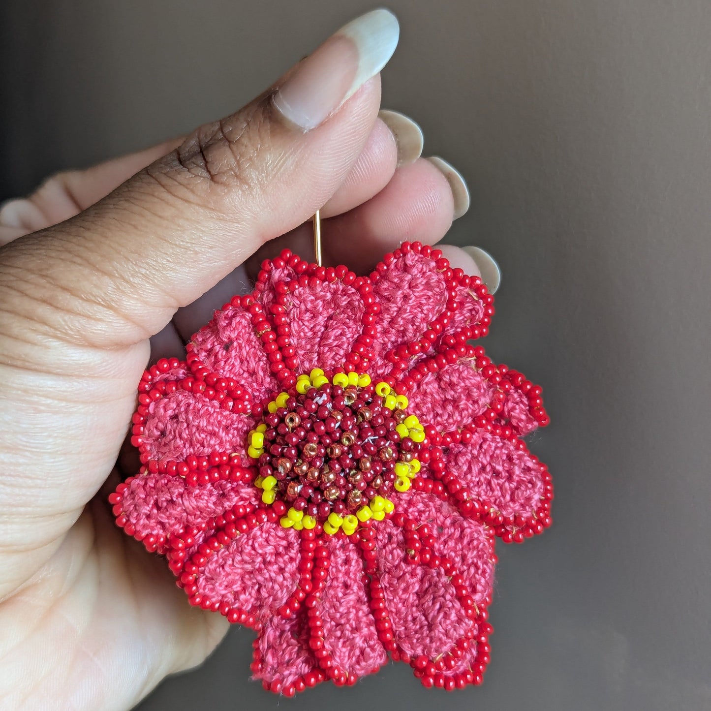 Zinnia flower brooch hat lapel pin by UK Indian designer and artisan Megha of Mayaani Jewellery held in hand against a neutral grey backdrop featuring Egyptian cotton and high quality glass seed beads.