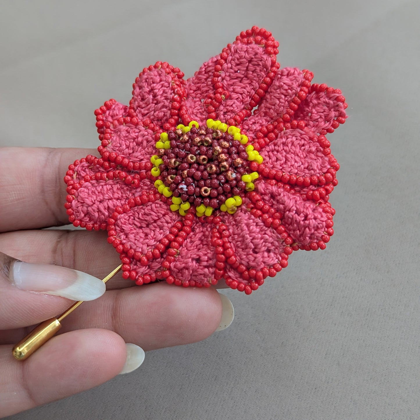 Hand holding a one of a kind sustainably handmade intricate brooch inspired by the Zinnia flower exclusively available from UK luxury jewellery brand Mayaani.